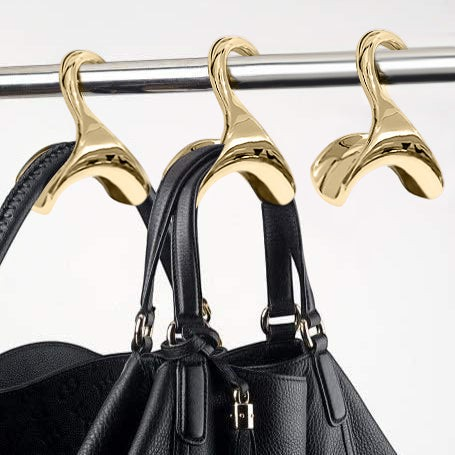 Bag-a-Vie gold metal handbag hangers with sculpted design to protect purse handles, shown hanging on a closet rod.